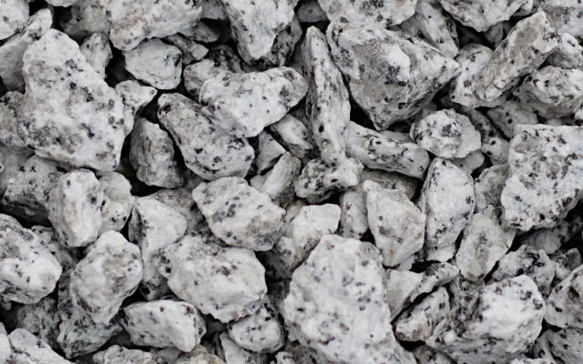 Taškuota granito skalda iš arti, šviesūs kampuoti akmenukai su tamsiais taškeliais