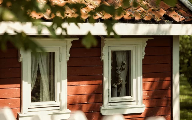 Raudonai dažytos horizontalios medinės dailylentės ir baltai apvadinti langai